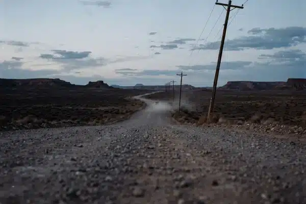 A car disappearing along a gravel desert road beneath telephone lines for Highway Lantern’s Static and Gravel
